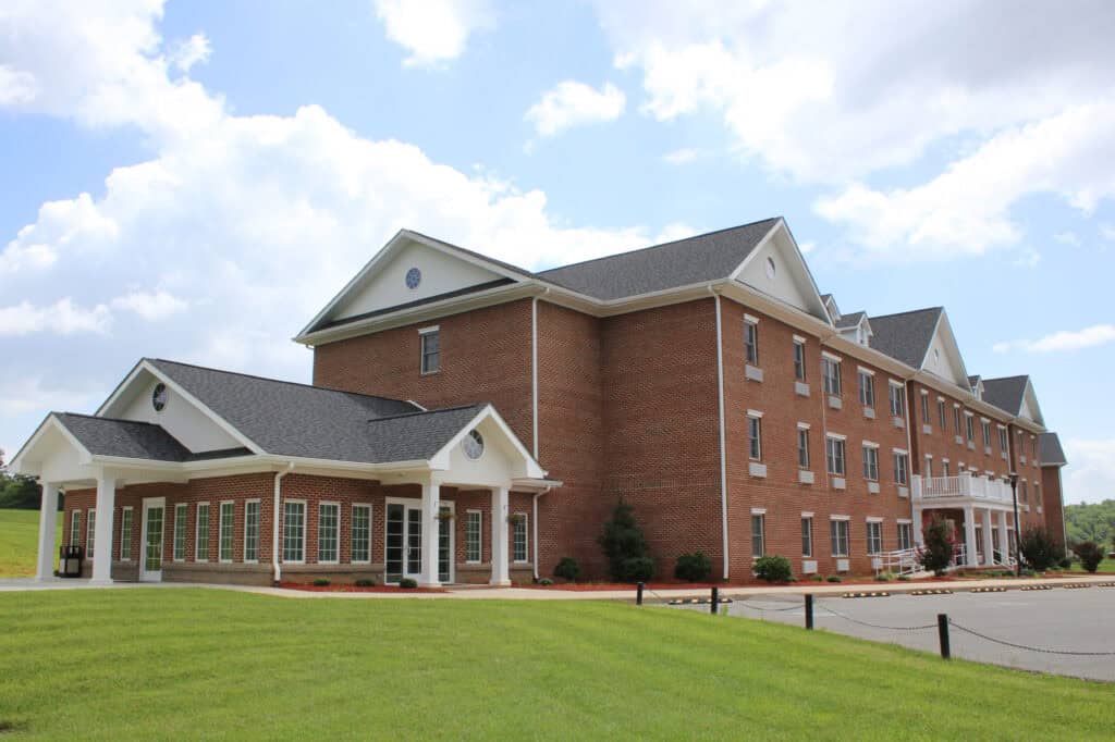 Pictured is Ferrum College Dyer Hall, a brick building with white trim with green grass and a blue sky with puffy white clouds
