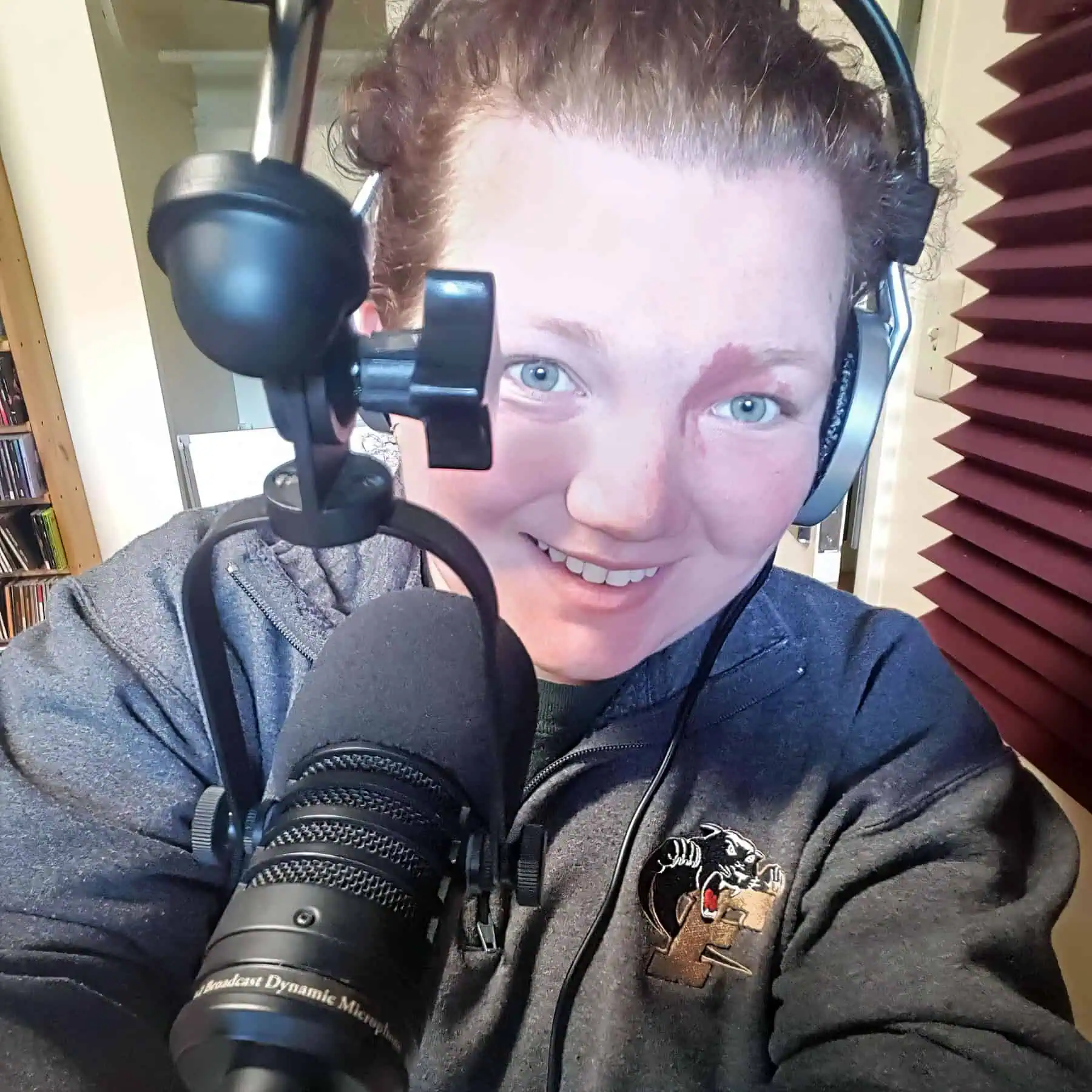 Photo of a woman in a gray sweatshirt with a panther logo wearing headphones in front of a radio microphone