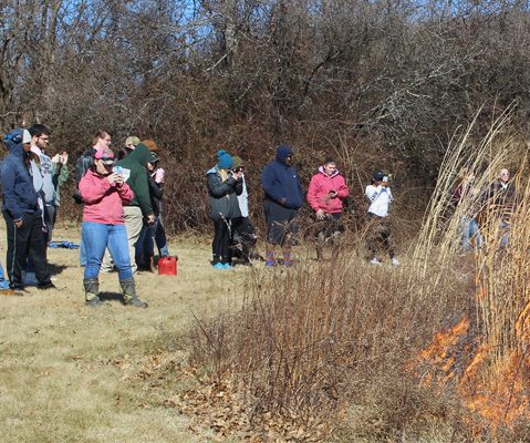 students outside in coats watching fire in field
