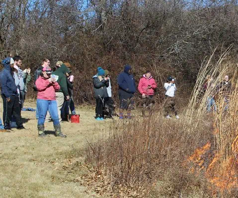 students outside in coats watching fire in field