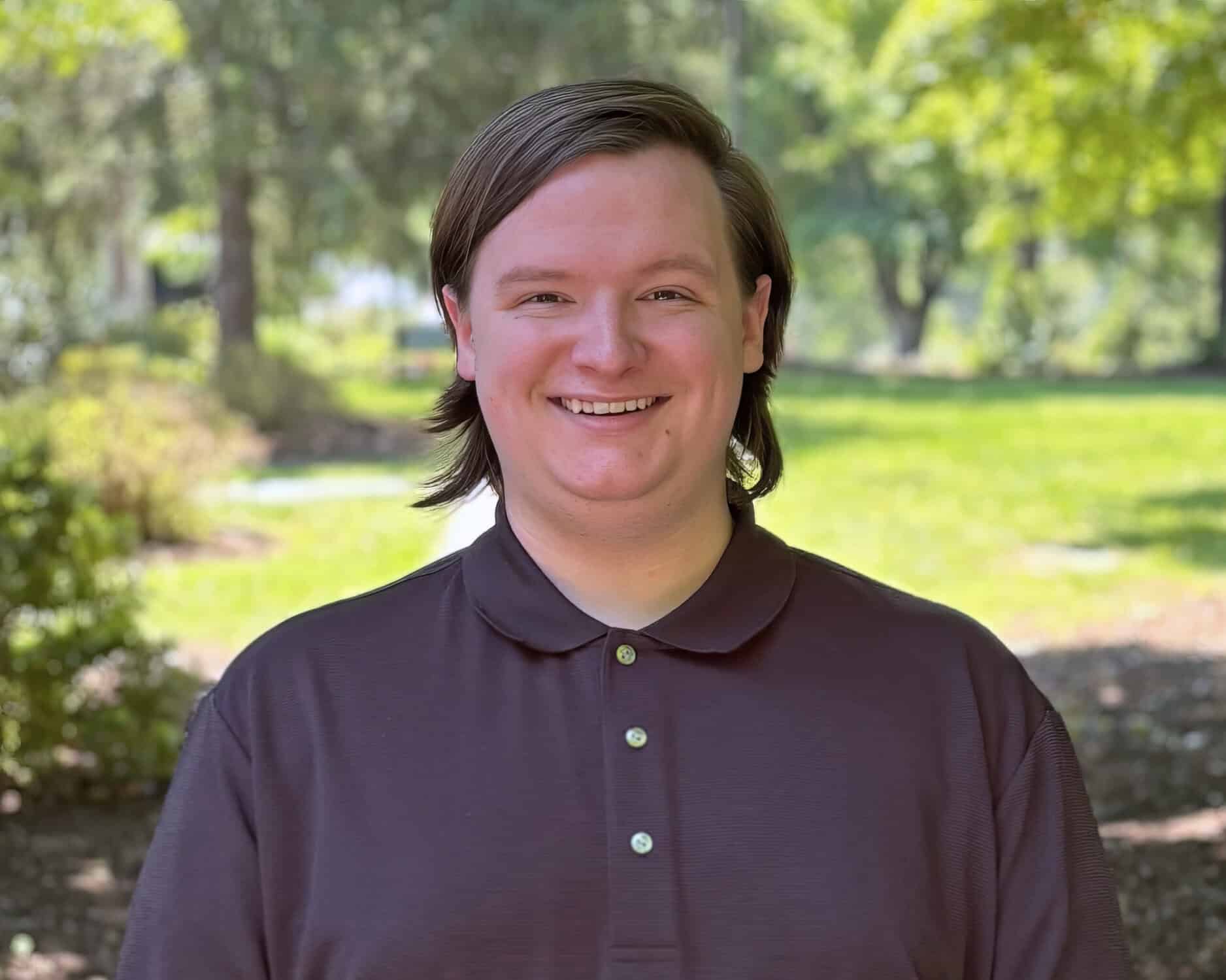 Gage Shelton headshot. Sunny day; he's standing in the shade with trees in the background.