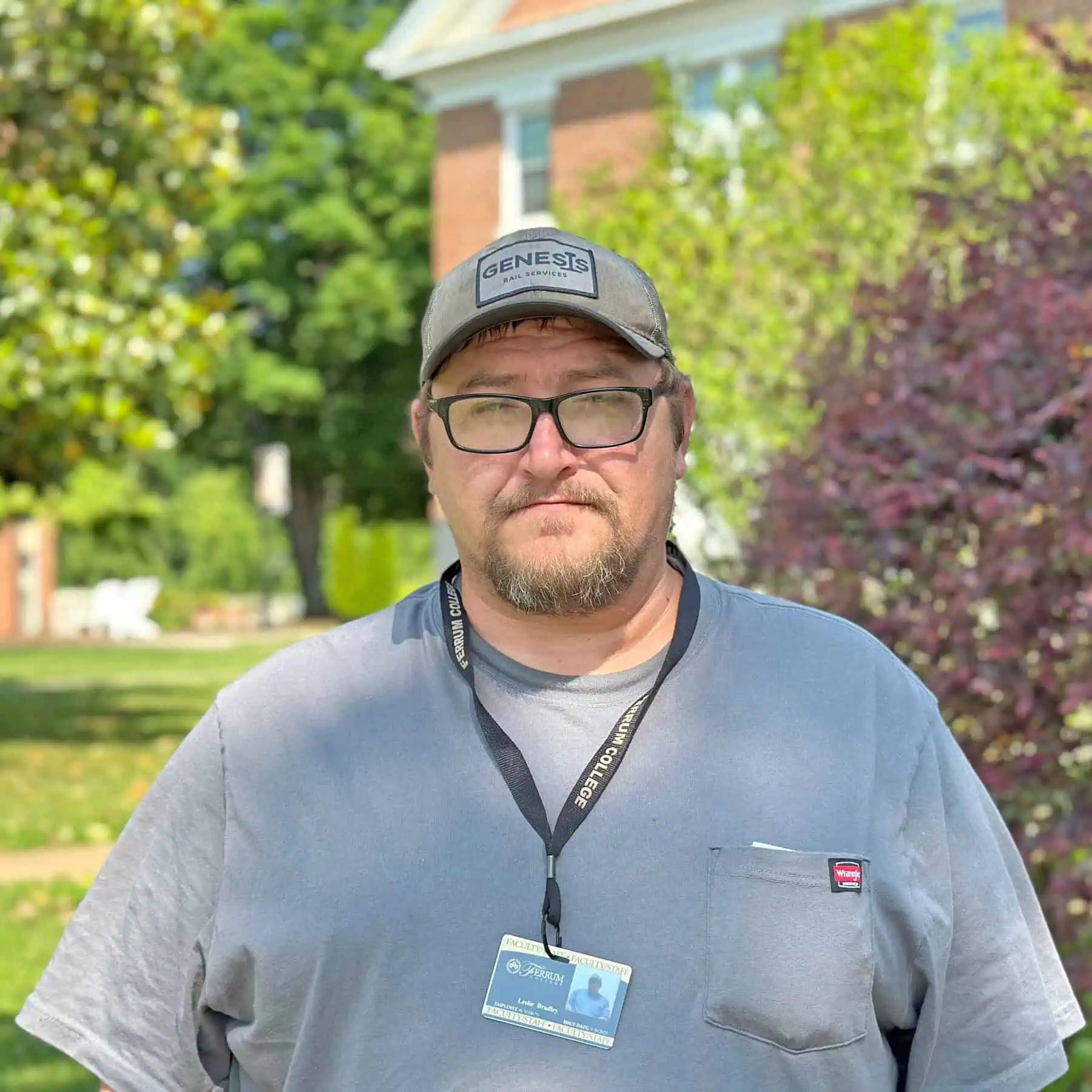The photo is of Leslie Bradley wearing a baseball cap and gray t-shirt taken outside on the Ferrum College campus on a pretty summer day