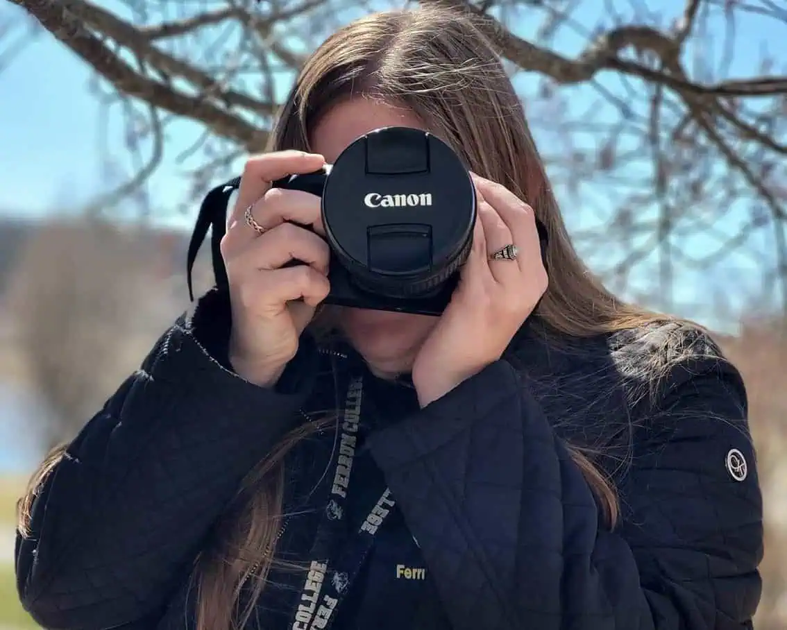 girl under tree branches while holding canon camera