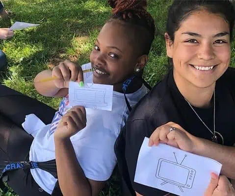 two female students holding up flash cards with drawings of televisions
