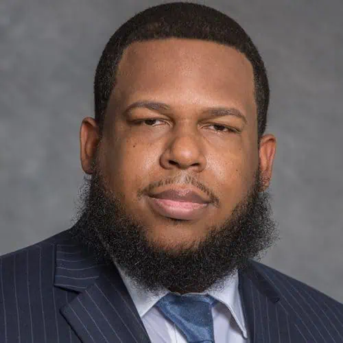 cornell sneed in black suit in front of gray background for staff photo