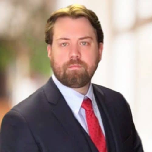 Headshot of Ferrum College professor Ryan Cooper who is wearing a dark suit, light colored shirt, and red tie