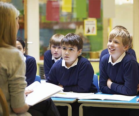 female teacher with a book in her hand facing male students in blue uniforms