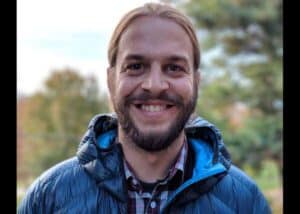 Man wearing a blue jacket is smiling brightly to the camera.