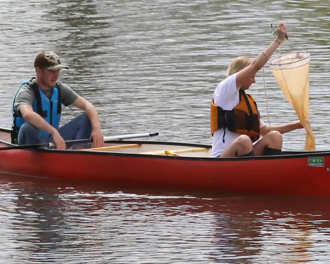 female and male student fishing with a net on a red kayak