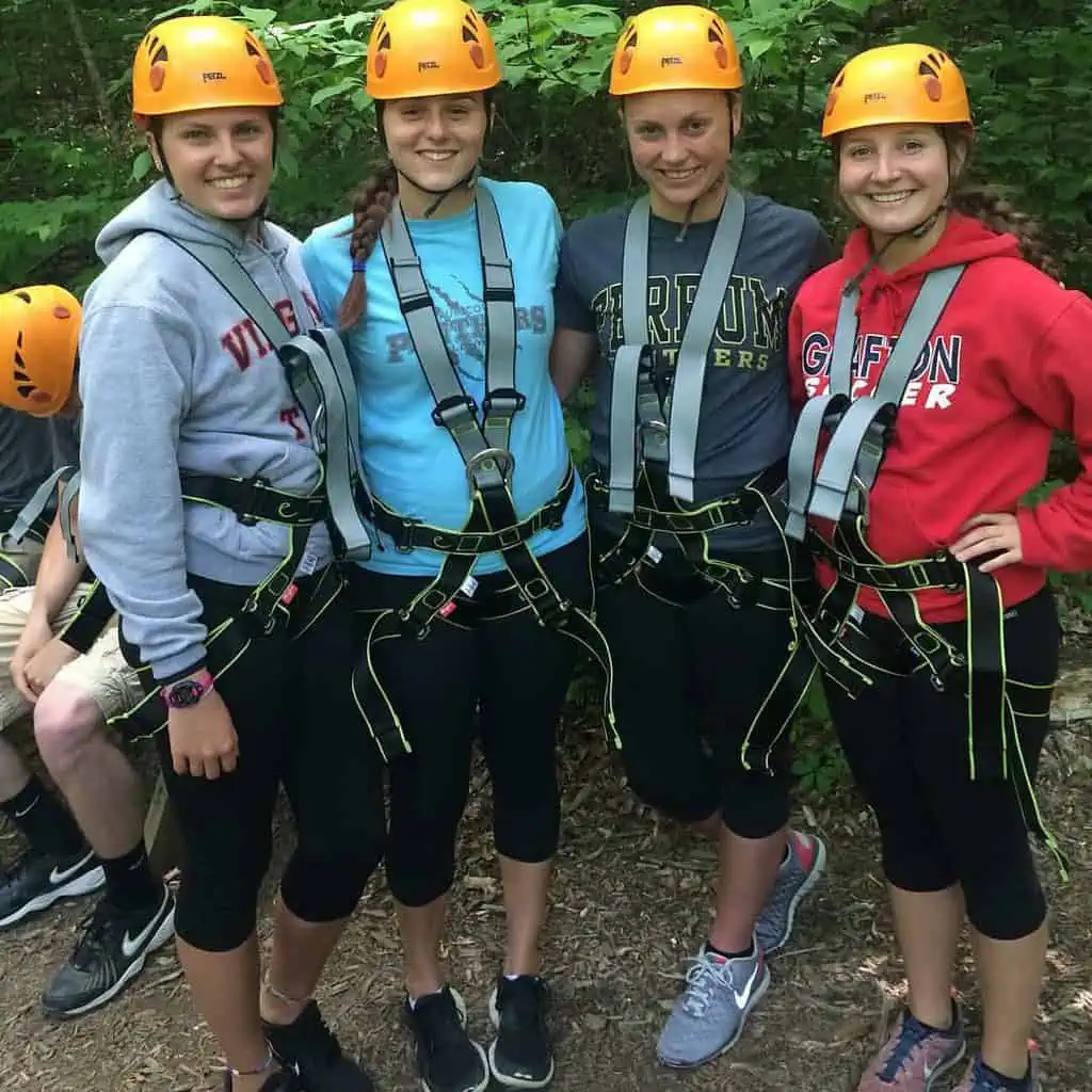 group of four female students in helmets and straps preparing to zip line