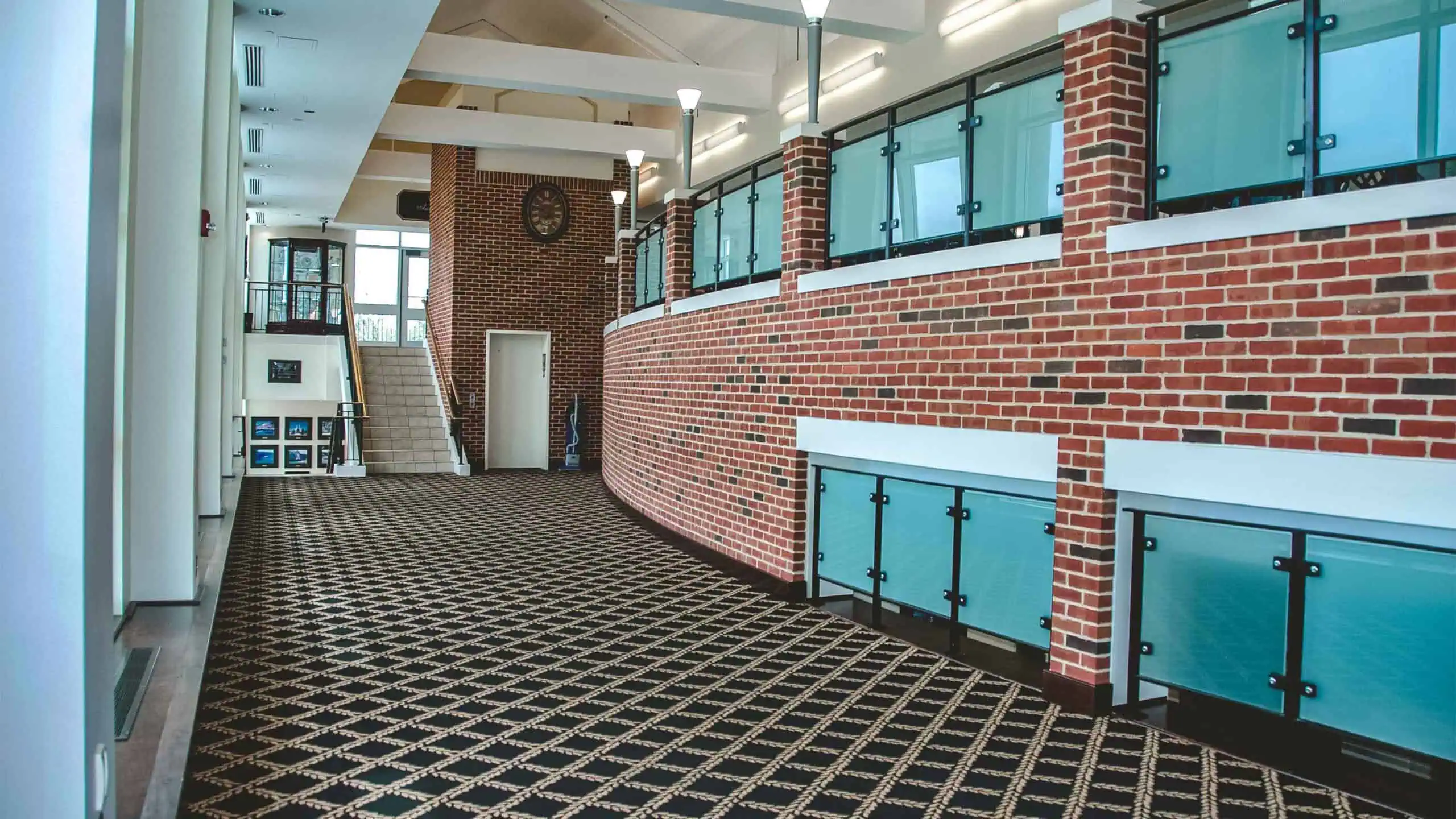 Atrium in Franklin Hall with curved red brick wall that has railing at top and bottom, stairs and elevator at back, black and gold carpet