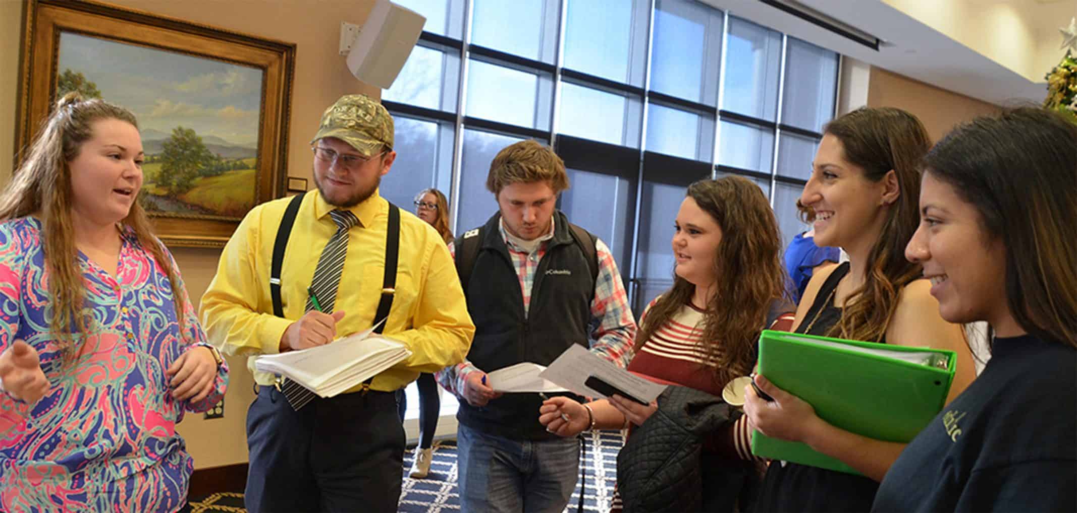 group of students standing while listening to a female advisor and looking at paperwork in the blue ridge mountain room