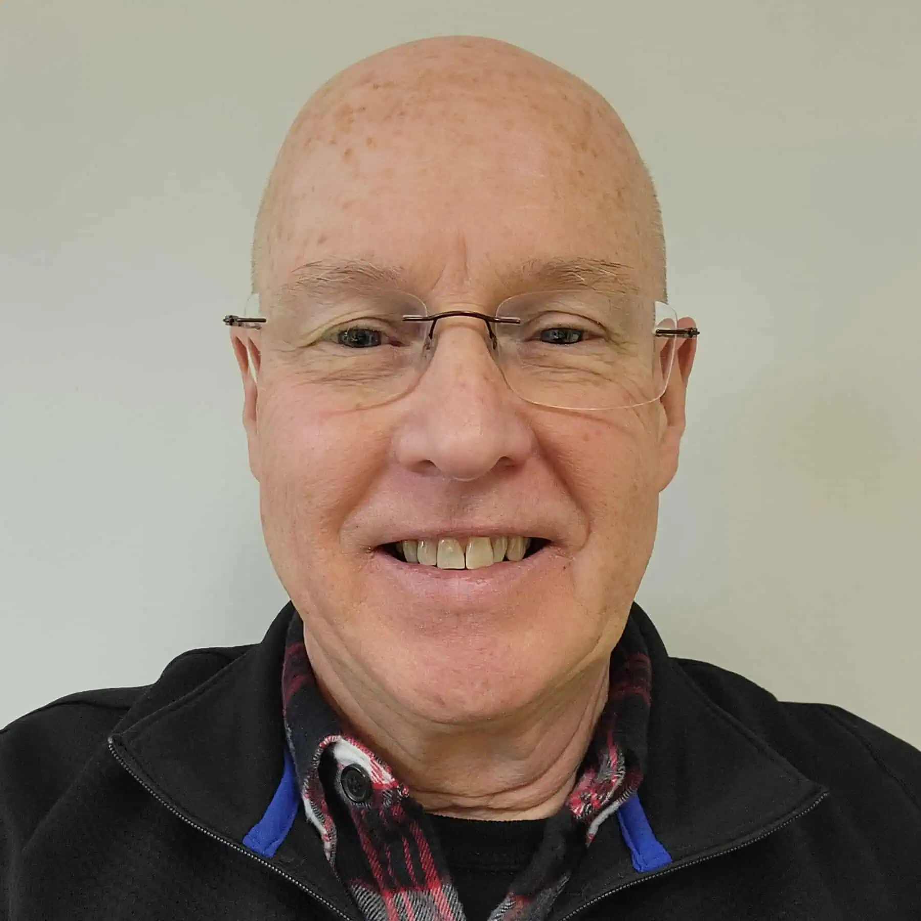 Photograph of a bald man wearing glasses, a plaid shirt, and a black fleece sweatshirt